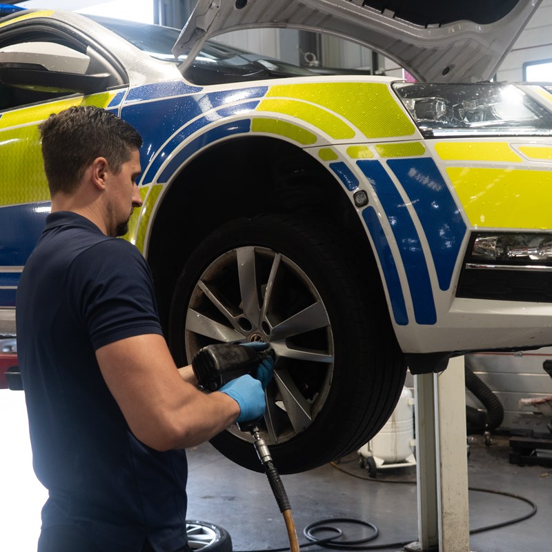 Vehicle technician taking the wheel nuts of a police car on a ramp in a workshop