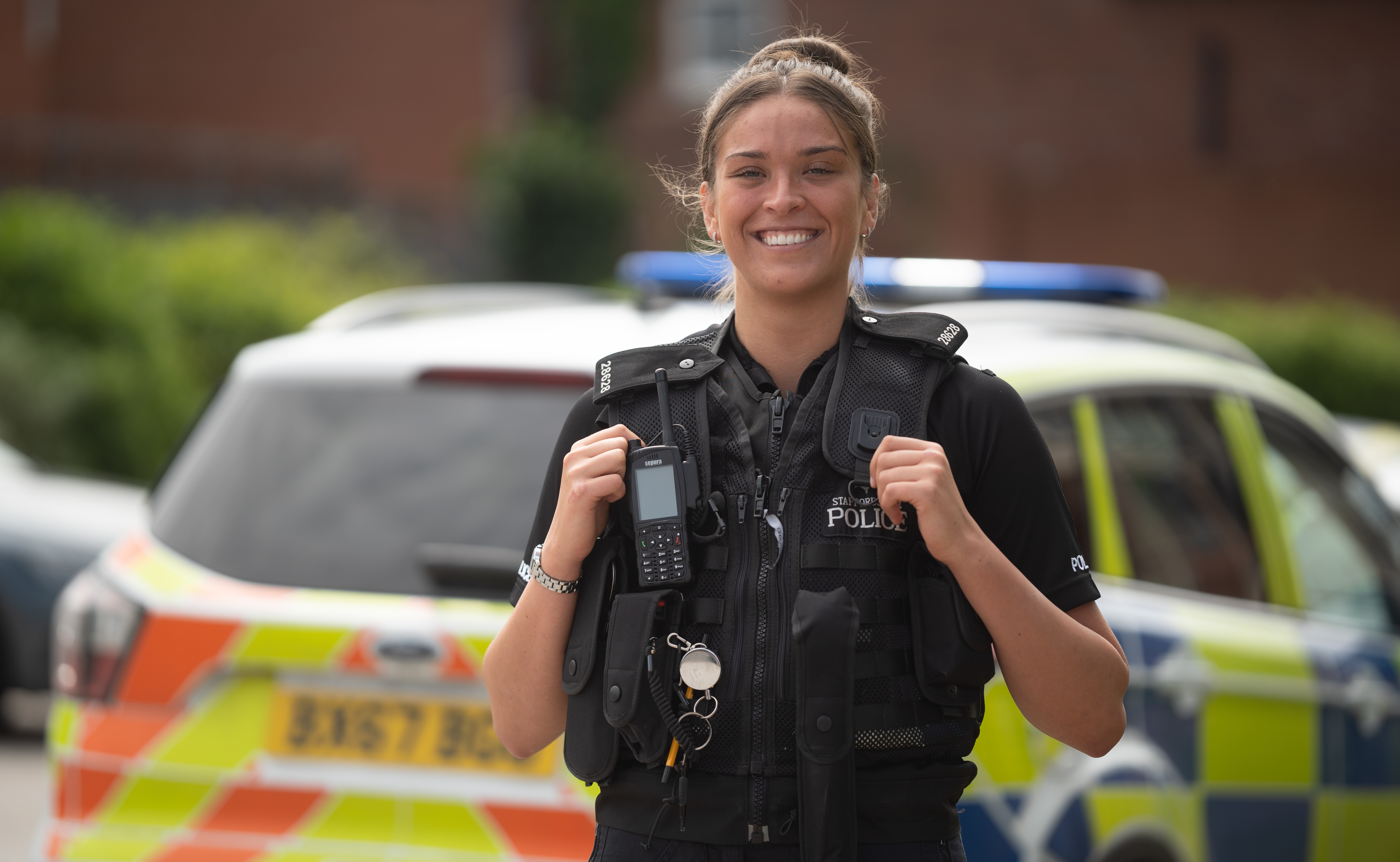Smiling female police officer looking into the camera and stood in front of a police car.